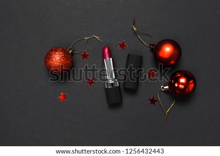 Red lipstick, Christmas balls, confetti on black background top view flat lay copy space. Professional Makeup and Beauty. Fashionable bright lipstick closeup. Make-up new year christmas concept. 