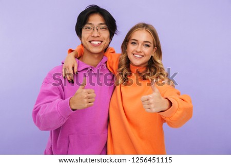 Photo of emotional young couple friends students standing isolated over white wall background showing thumbs up.