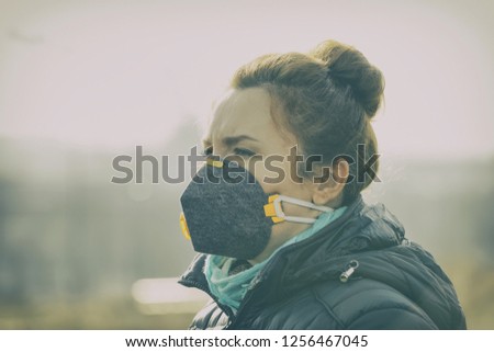 Woman wearing a real anti-pollution, anti-smog and viruses face mask; dense smog in air. Royalty-Free Stock Photo #1256467045
