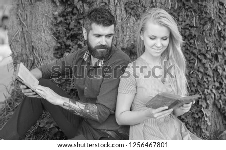 Romantic couple holds old books with poems. Date and love concept. Couple in love sits outdoor with old books, nature background, defocused. Girl with happy face and bearded man reading poems.