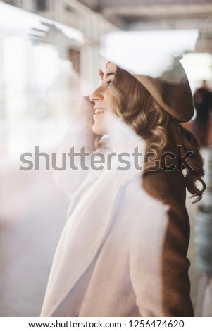 Attractive woman in total beige look wears beret and coat. Curly hair. Woman under the glass of window. Photo in the style of the old movie