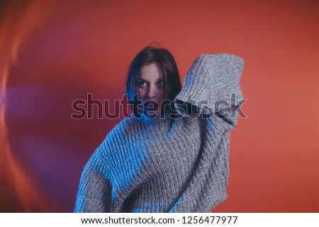 Young girl in warm grey sweater posing on orange background, woman with short haircut in knitted sweater, space for text