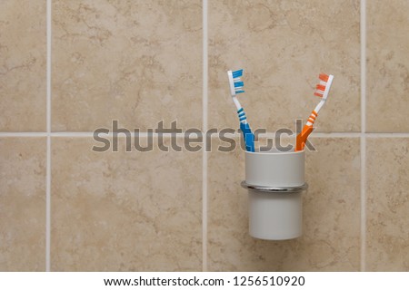 Toothbrushes in plastic cup holder on a tiled wall in a bathroom closeup