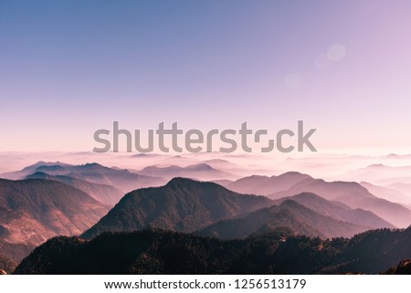 View of Himalayas mountain range with visible silhouettes through the colorful fog from Khalia top trek trail. Khalia top is at an altitude of 3500m himalayan region of Kumaon, Uttarakhand, India. Royalty-Free Stock Photo #1256513179