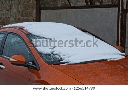 part of a brown car with snow and frost on the windshield