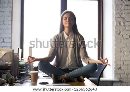 Serene calm business woman sit on office desk taking break for meditation, mindful employee doing yoga exercise in lotus pose for relaxation at workplace, no stress relief, balance at work concept Royalty-Free Stock Photo #1256562643