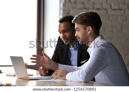 Financial advisor insurer speaking consulting african client looking at laptop making presentation, caucasian mentor teaching black intern, employees colleagues help discuss online computer project Royalty-Free Stock Photo #1256570881