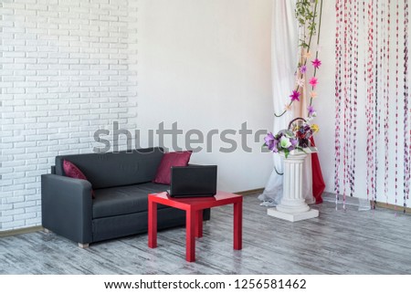 Beautiful interior in retro style. Beautiful and minimalistic interior with a white brick wall, a black sofa with a red coffee table and a pillar with decor.