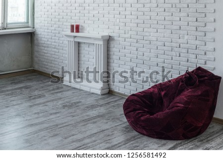 Beautiful interior in the style. Beautiful and minimalistic interior with a white brick wall, white fireplace and a red rag chair bag.