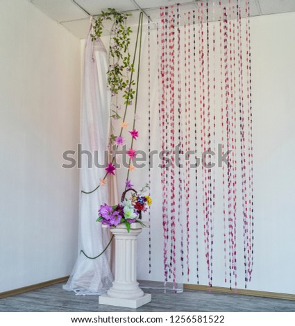 Beautiful interior in retro style. Beautiful and minimalistic decor with a white column and flowers on it with bright and red threads and vertical vines against a white interior.
