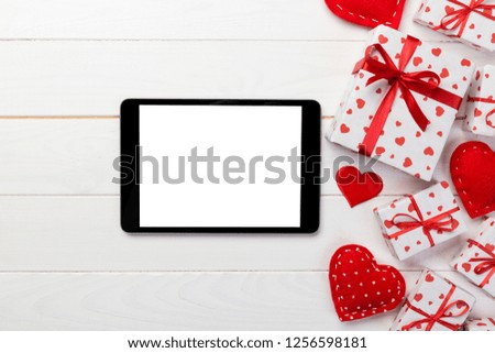 Digital tablet blank screen with gift box and hearts decor on wooden table. Top view. Valentines Day concept background.