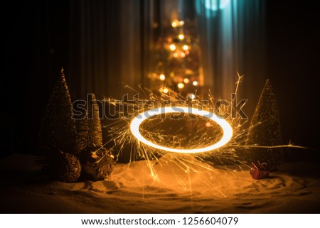 Glittering burning sparkler on snow with blurred Christmas tree on dark background. New Year Holiday concept with empty space for your text. Selective focus