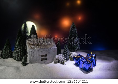 Christmas and New Year miniature house in the snow at night with fir tree. Little toy house on snow with tree. Festive background. Christmas decorations. Holiday concept.