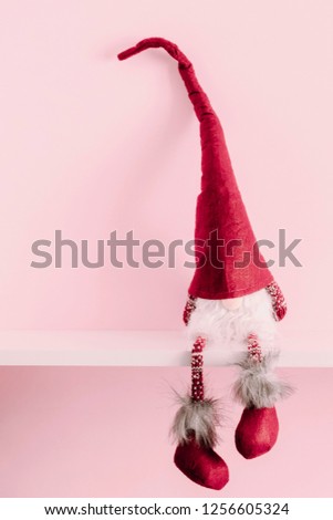 Red sitting christmas elf with pointed cap on white shelf and pink wall
