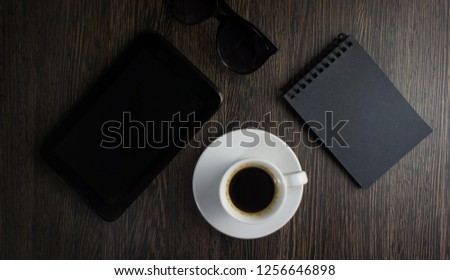 Business workspace dark key. Business tablet, cup of coffee, notebook. Selective focus, top view. Flat lay.