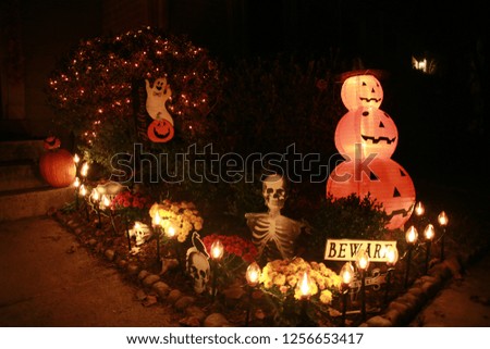 Skeleton in Flower Bed with Beware Sign Guarding Front of Townhomes with Plastic Pumpkins Ghost and Other Decorations on Halloween at Night