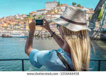 Happy blonde woman - tourist shot on her smartphone camera beautiful city view. with ships on the river in sunny day.