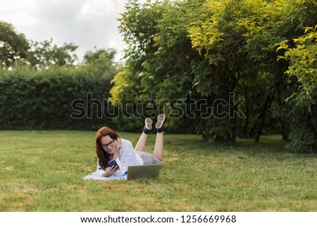 Business woman lying on a green grass and working using her laptop.