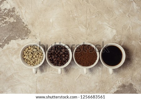 four types of coffee unroasted, bean, ground and one in cup top view.
