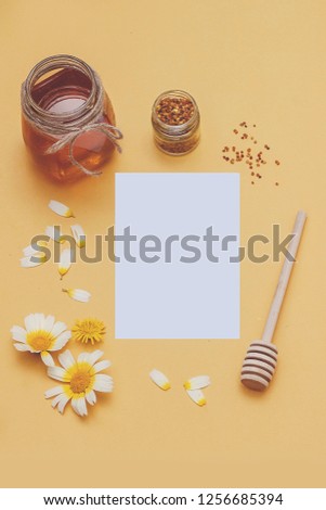 Blank paper between honey, flowers and honey spoon in yellow background