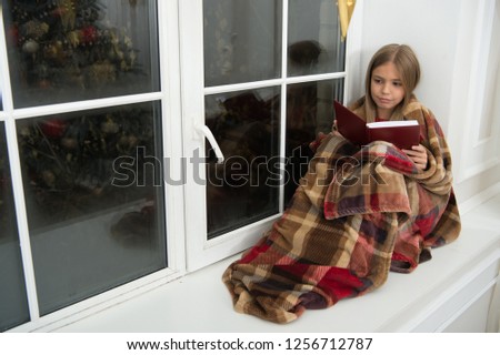 Happy Holidays. Little child read book on Christmas eve. Little girl enjoy reading Christmas story. Little reader wrapped in plaid sit on window sill. Childrens picture book. Magic xmas spirit.