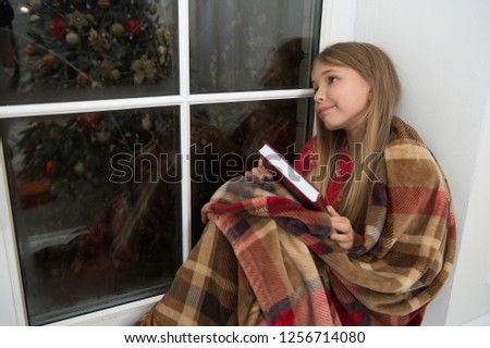 Cute dreamer. Small child read book on Christmas eve. Small reader wrapped in plaid sit on window sill. Childrens picture book. Magic xmas spirit. Small girl enjoy reading Christmas story.