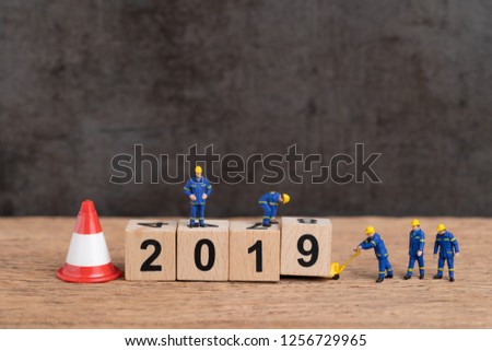 Year 2019 new year changing or just finished concept, miniature people workers building cube wooden block number 2019 with under construction sign and traffic cone, dark background with copy space.