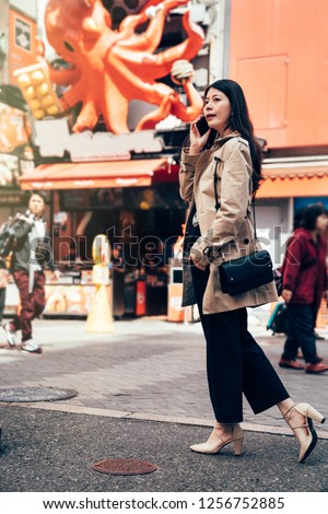 full length of young office lady talking on smartphone asking the direction of client company going to visit. elegant asian woman standing in front the takoyaki shop with big octopus hanging on wall