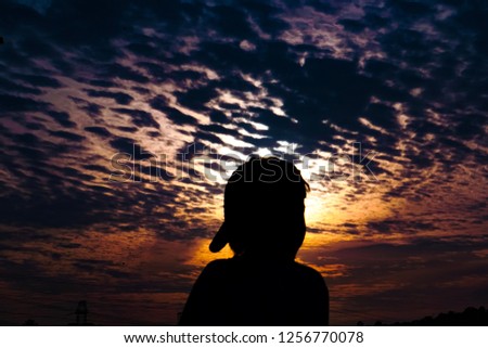 Boy in baseball hat cap looking over colorful sunset sky clouds