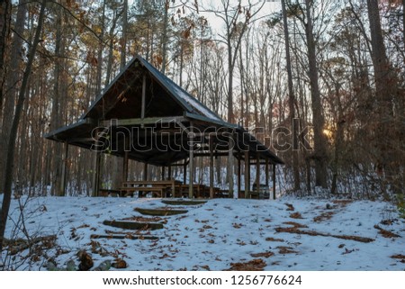 The fading sun peeks at an outdoor classroom nestled in the woods with the remnants of snow on the ground at Yates Mill County Park in Raleigh, North Carolina.