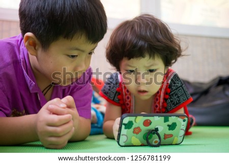 two chinese children addicted tablet, asian child watching tablet, kid use telephone together on their bed, play phone, kid addict smartphone
