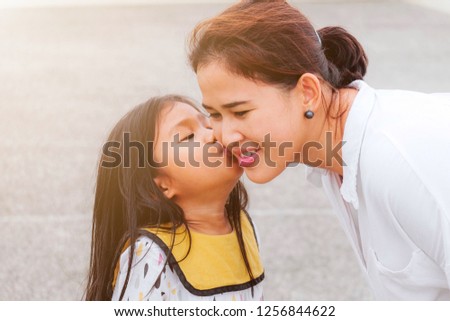 A cute daughter kissing her mom on cheek with sun light effect.