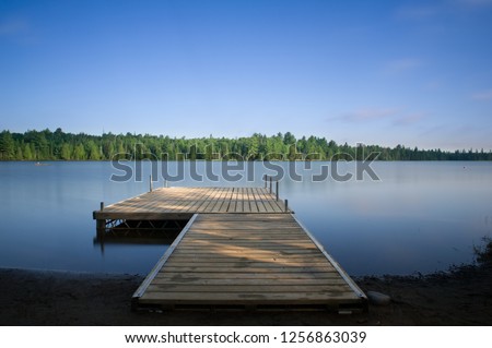 Wooden dock on a calm lake at the cottage in Ontario, Canada. Royalty-Free Stock Photo #1256863039