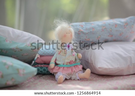 Handmade textile toys are a tender doll for a girl with blond hair and in a beautiful dress on pillows. Nature photography