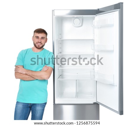Young man near empty refrigerator on white background