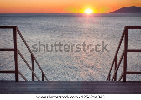 Stairs leading into the sunset. Seascape, lens flare 35 mm.