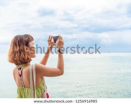 Beautiful asian woman with short hair using smartphone take a photo seascape view with copy space.