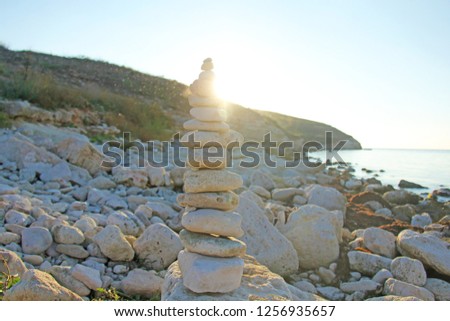 Stone tower on the beach on the background of the sea and the sun.