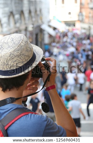 Caucasian boy with a hat photographs people walking on the street