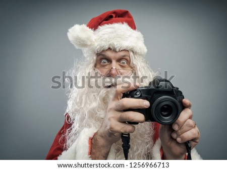 Happy surprised Santa Claus holding a camera and shooting holiday pictures for Christmas