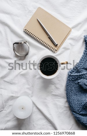 Cup coffee , blue knitted sweater, notebook with pen,  clock, candle on bed, top view. Women clothing. Flat lay, cozy concept