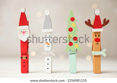 Creative holiday clothespins in form of Christmas tree, snowman, Santa Claus and deer on neutral background with yellow lights.