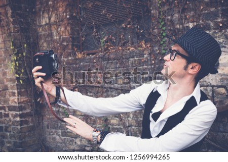 Fedora styled smiling man taking selfie with vintage medium format photo camera. 