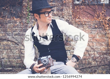 Pensive retro styled man holding vintage analog photo camera against brick wall. 