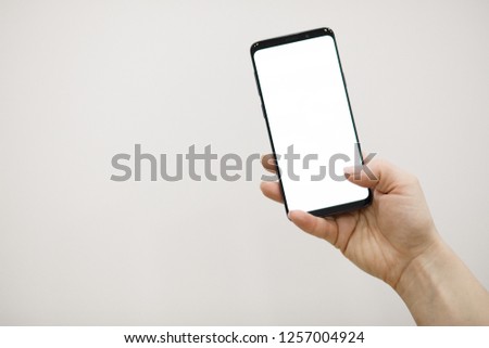Female hand holding black cellphone with white screen close up. Woman's hand holding a smartphone isolated on white background.