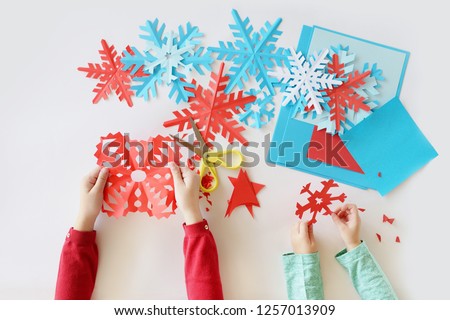 top view. Children's hands cut out on a white background blue and red snowflakes from paper Royalty-Free Stock Photo #1257013909