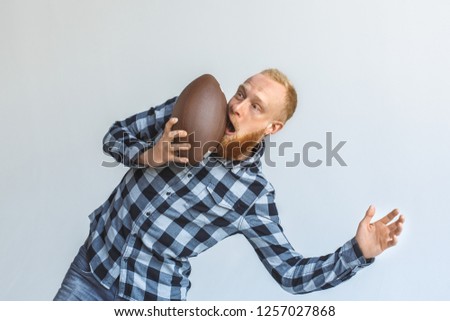 Red hair mature man bending aside isolated on grey wall hit the face with american football ball mouth opened unexpected