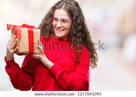 Young brunette girl holding a gift over isolated background with a happy face standing and smiling with a confident smile showing teeth