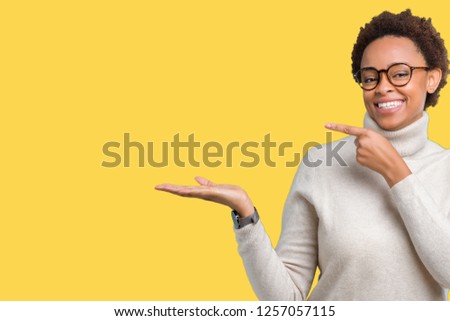 Young beautiful african american woman wearing glasses over isolated background amazed and smiling to the camera while presenting with hand and pointing with finger.
