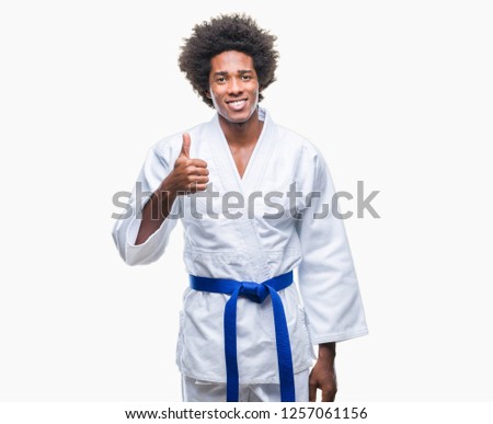 Afro american man wearing karate kimono over isolated background doing happy thumbs up gesture with hand. Approving expression looking at the camera with showing success.